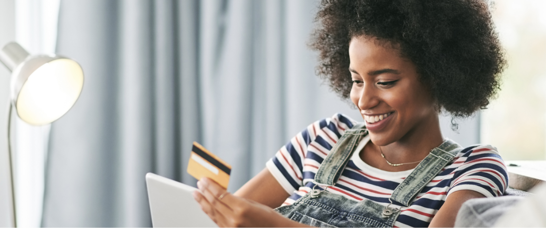 Smiling woman holding up credit card as she makes online purchase on laptop.