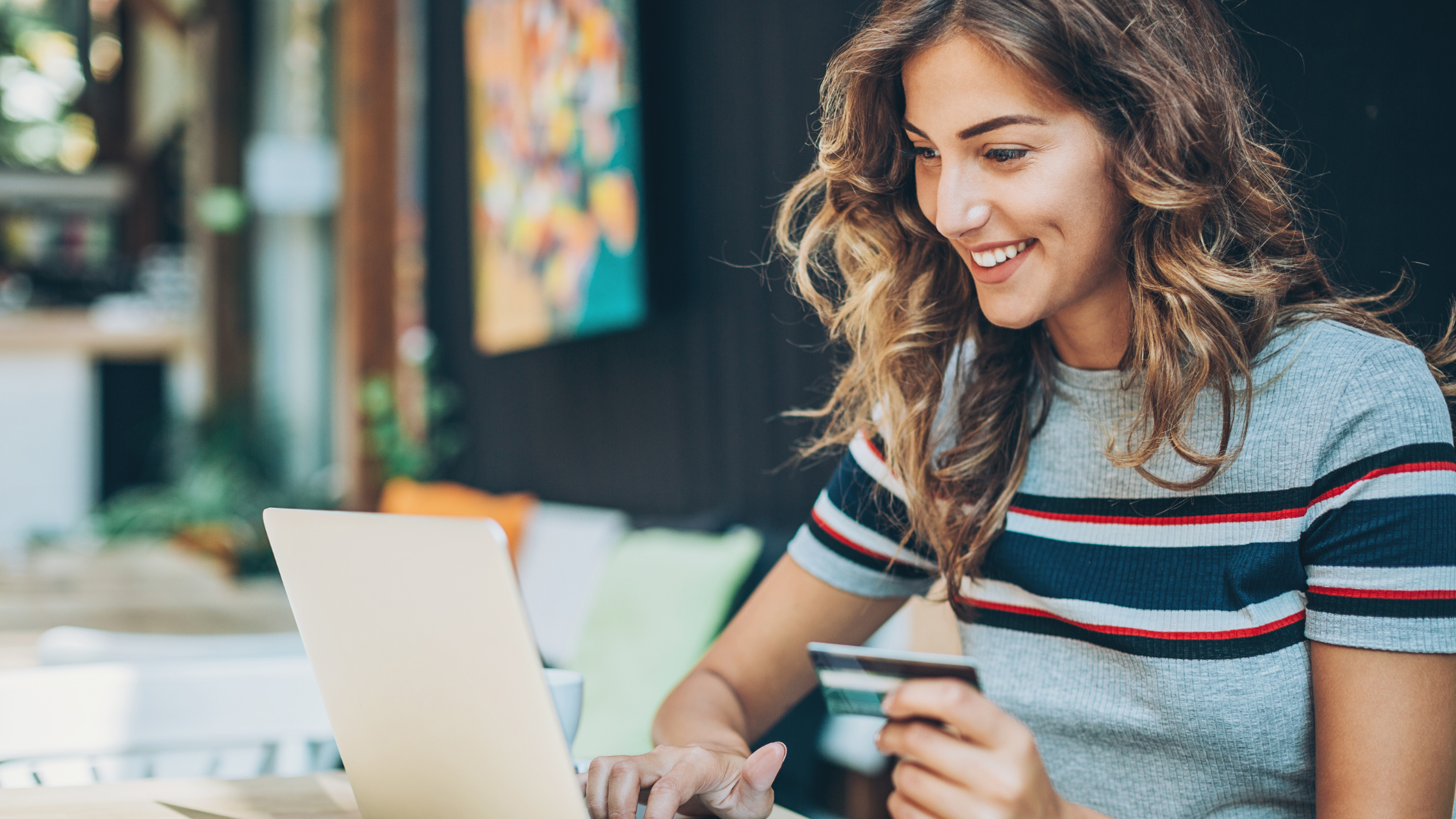 blond woman in front of laptop smiling at the screen with her payment card in hand